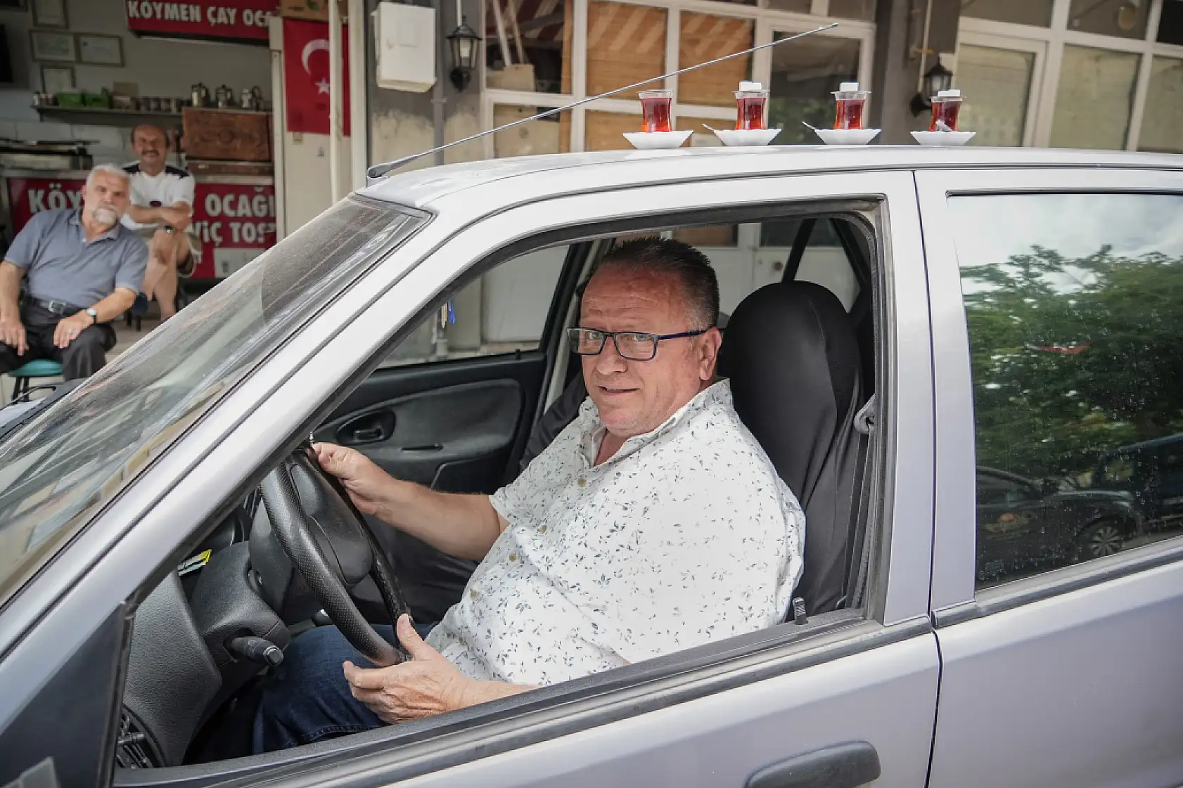 50 metre uzaklıktaki çay ocağından aldığı çayları otomobiliyle taşıyor